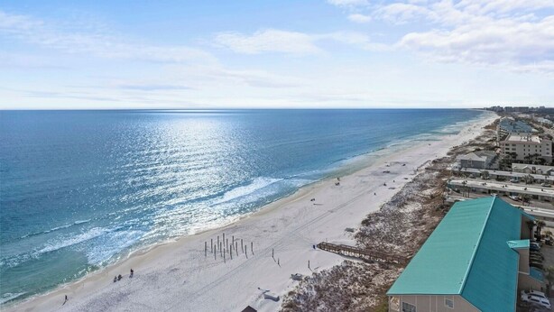 A coastal hotel with a beach view, a long pier, and a clear sky.