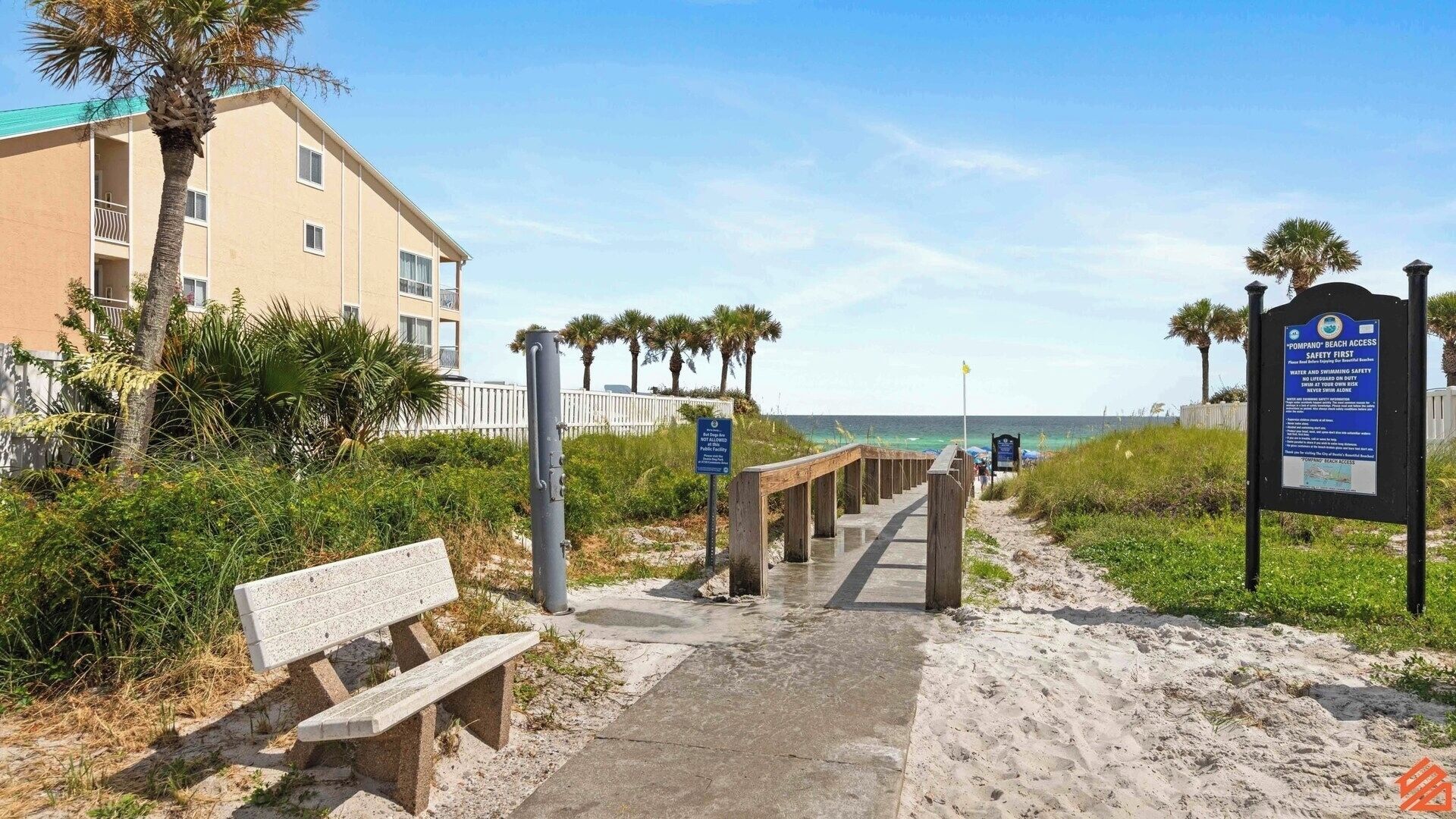 A beach access sign with safety instructions, a wooden walkway leading to the beach, and a bench.