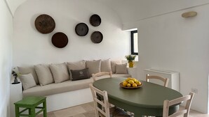 A dining area with a round table, chairs, a sofa, and decorative plates on the wall. - Trullo Il Nuciareddo (Ostuni)
