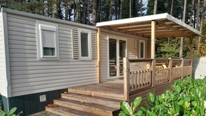 A mobile home with a wooden deck, a covered porch, and a small garden area. - Breebos Chalet Near Antwerp Camp (Rijkevorsel)