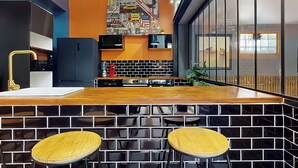 Une cuisine moderne avec un bar en bois, un dosseret carrelé en noir et blanc et deux tabourets.