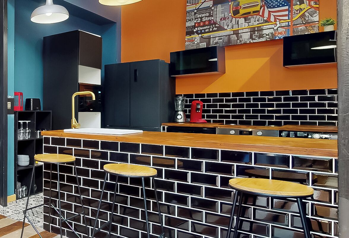 A modern kitchen with a black and white brick backsplash, a wooden bar counter, and three stools.