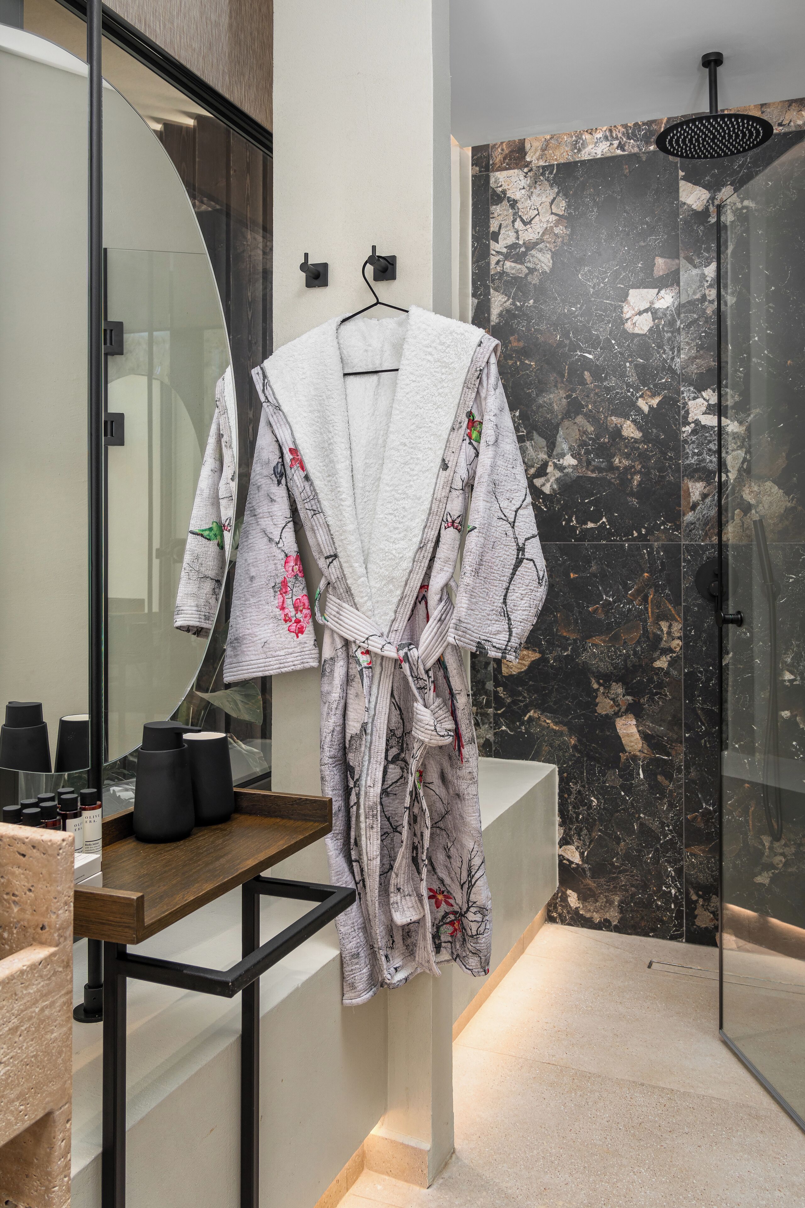 A bathroom with a glass shower enclosure, a large mirror, and a wooden vanity with toiletries.