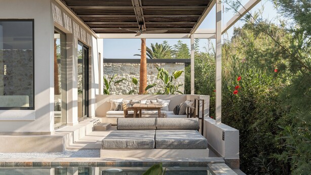 A modern outdoor seating area with a pool, stone walls, and lush greenery. - Dyo Beach Suites (Rethymno)