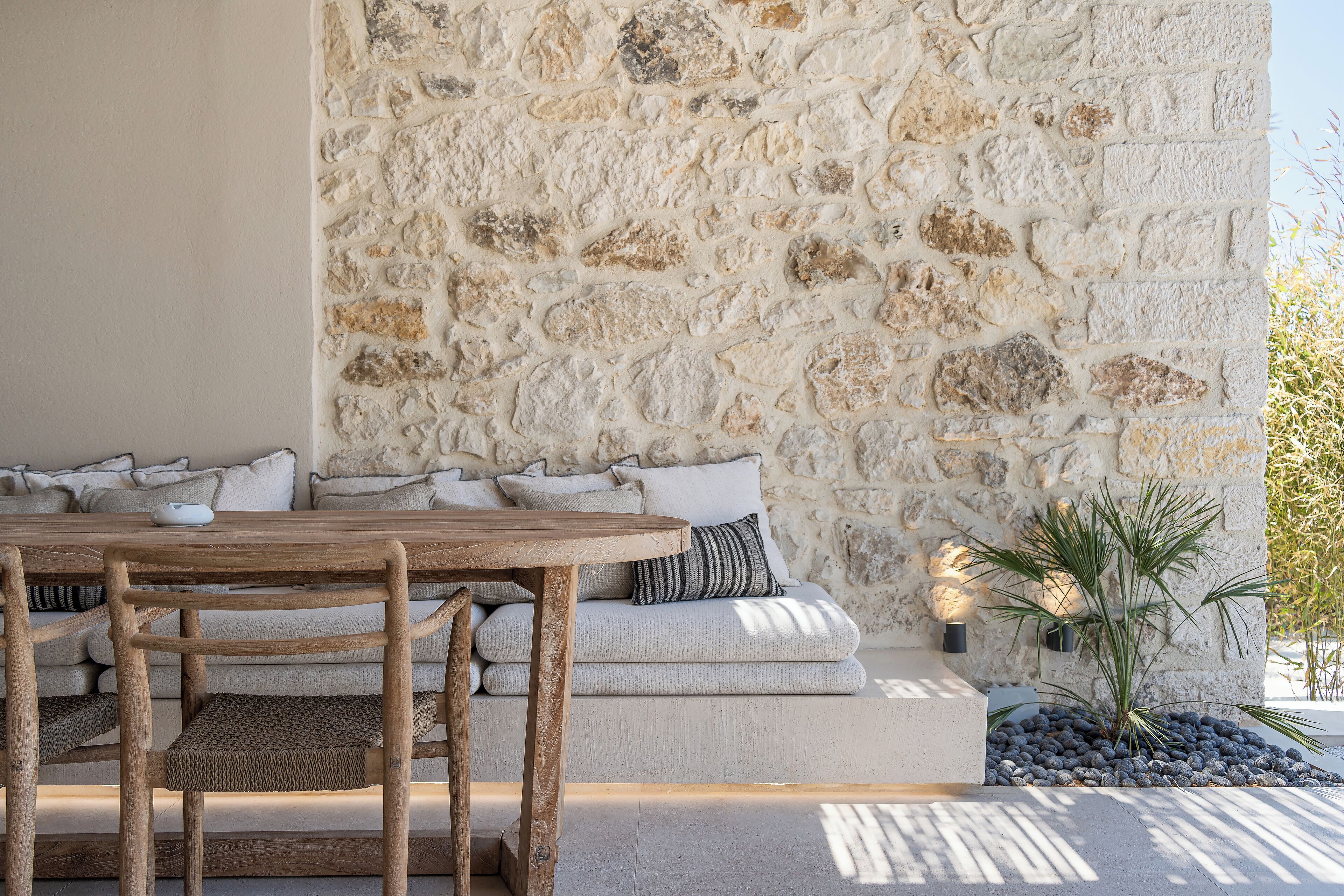 Un muro de piedra, una mesa de madera y un sofá con cojines.