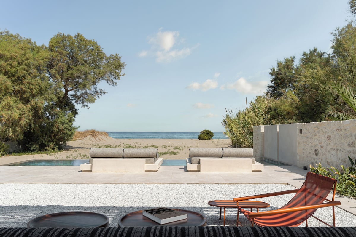 A poolside area with a view of the beach, outdoor seating, and a book on a table.