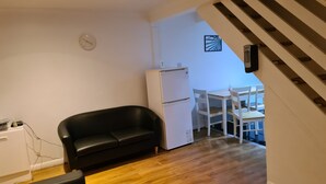 Un espacio habitable compacto con un sofá negro, un refrigerador blanco y una zona de comedor con sillas blancas.