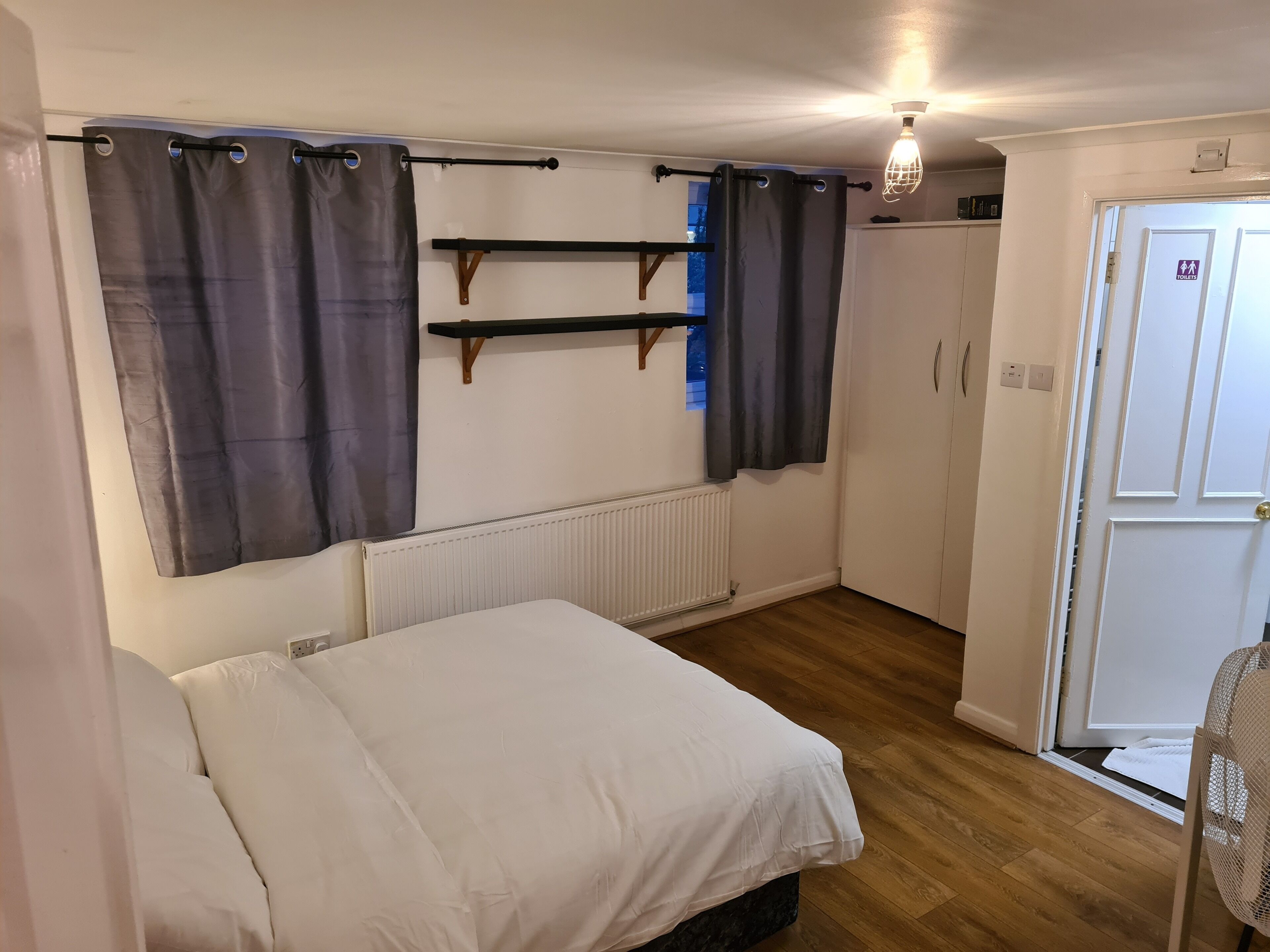 A bedroom with a bed, a radiator, a door with an exit sign, and a ceiling light fixture.