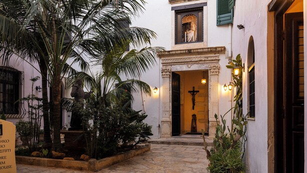 A courtyard with a stone floor, palm trees, and a statue. - Sundial Lodge (Chania)