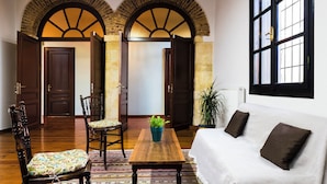A room with a wooden floor, a white sofa, a wooden table, and a chair. There is a plant on the table and a window with a view. - Sundial Lodge (Chania)