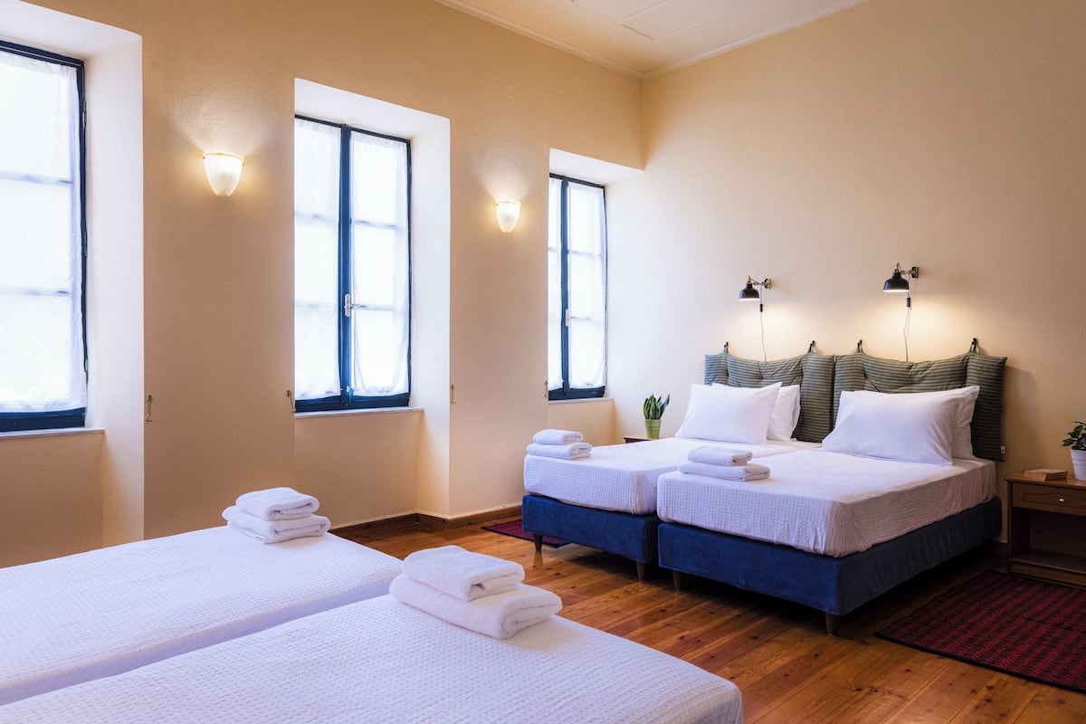 A hotel room with two single beds, a double bed, and a small table.