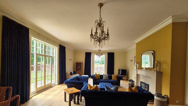 A spacious living room with a large blue sofa set, a wooden coffee table, and a chandelier.