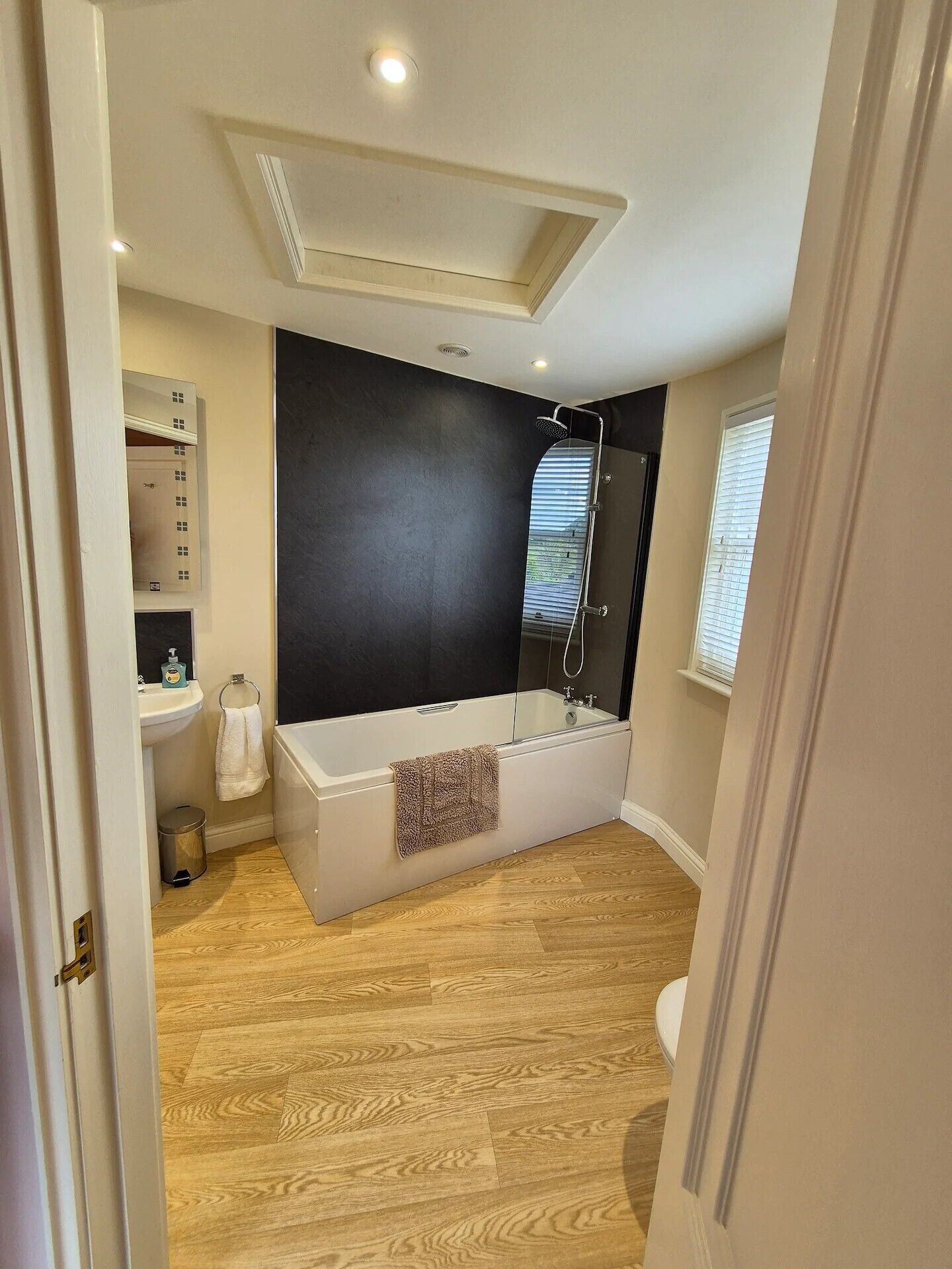A modern bathroom with a freestanding bathtub, a vanity with a mirror, and a window with blinds.