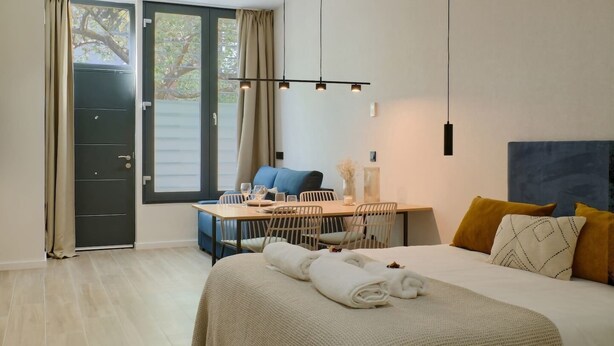Un dormitorio moderno con cama, escritorio y silla. Se ve una ventana con cortinas, una puerta y una lámpara colgante.