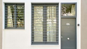 Fachada de edificio con un gran ventanal de barrotes horizontales, una puerta con la inscripción '06' y un ventanuco encima de la puerta.