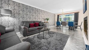 A living room with a grey sofa, red cushions, a round coffee table, and a patterned wallpaper.