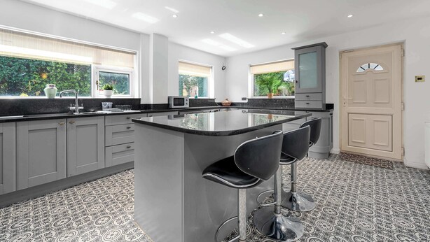 A modern kitchen with grey cabinets, a central island with bar stools, and large windows with blinds.