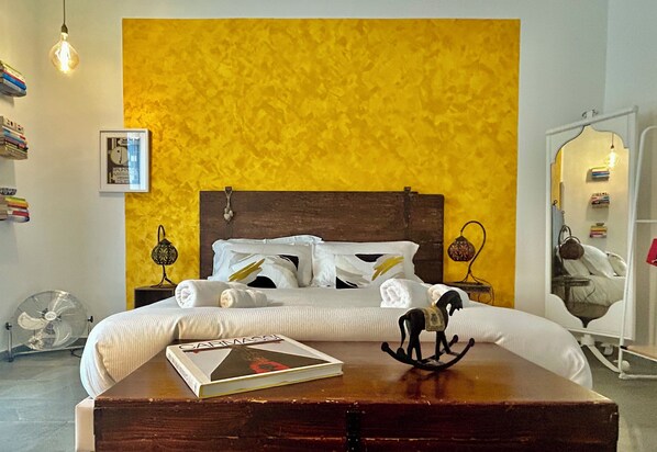 Une chambre à coucher avec un lit, des lampes de chevet, une table de chevet avec un livre, un ventilateur et un miroir.