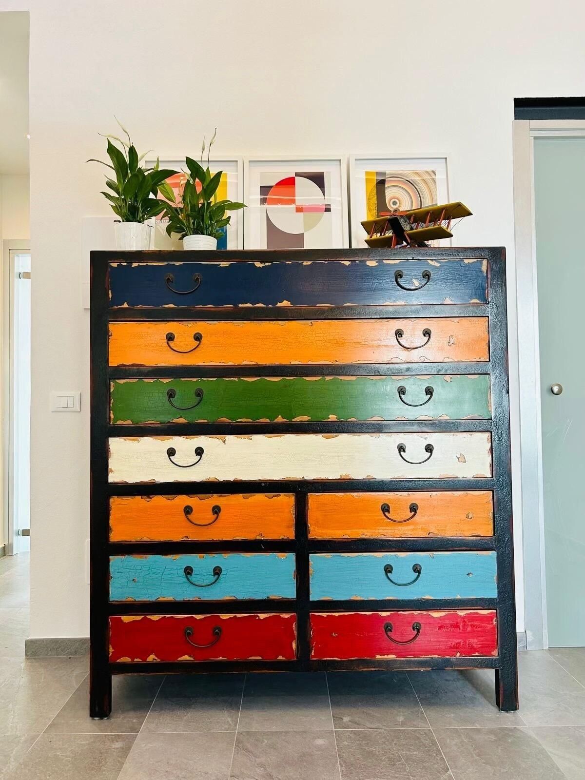 A multi-tiered wooden dresser with variously colored drawers, each with a handle.