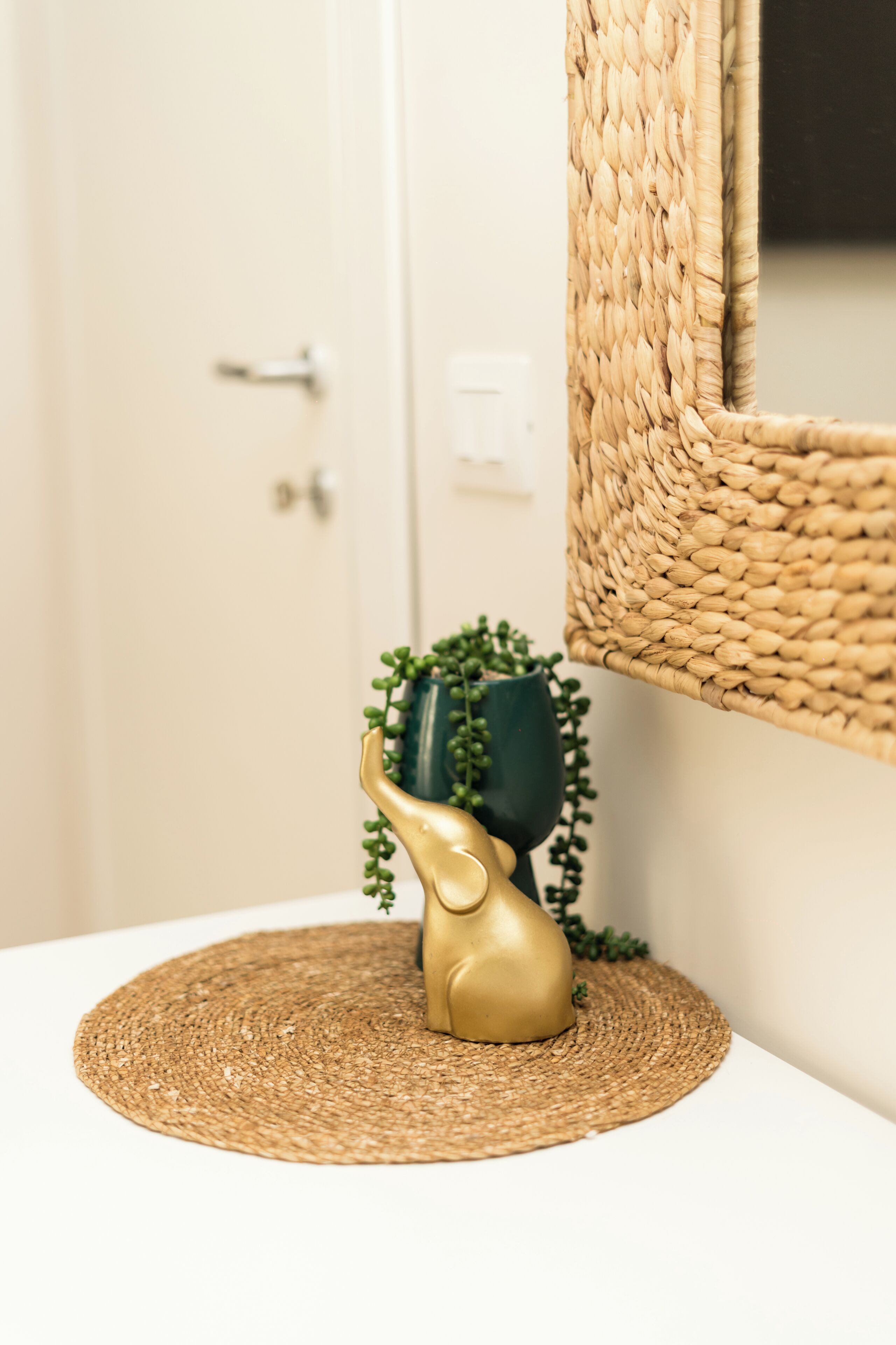 A bathroom with a white door, a woven basket, and a golden vase with a plant.