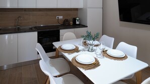 Eine moderne Küche mit weißen Schränken, einem eingebauten Backofen und einem Essbereich mit einem weißen Tisch, gedeckt für vier Personen.