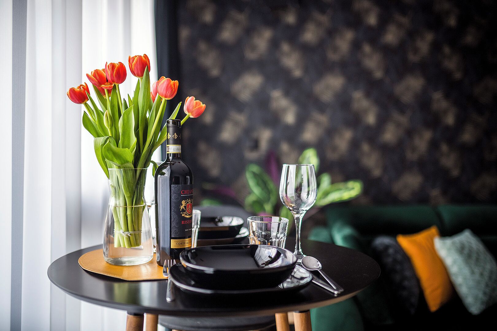Une table à manger avec une bouteille de vin, un verre et un vase de tulipes.