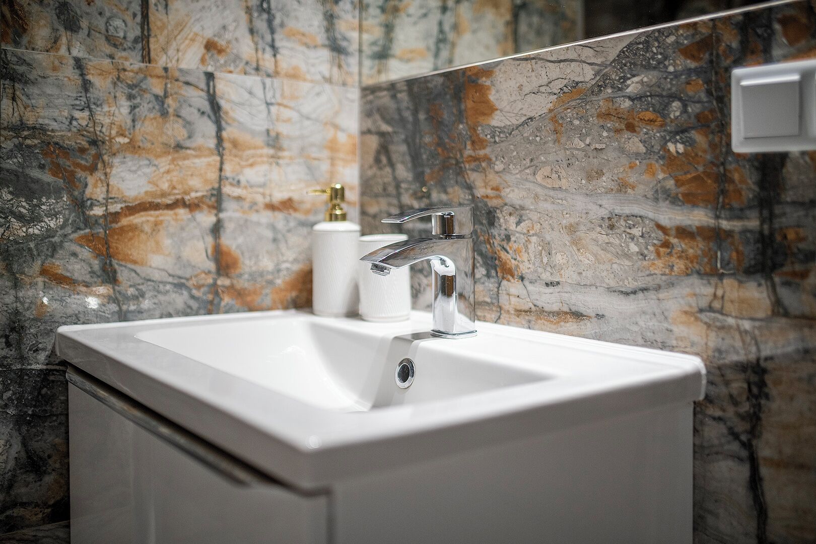 A bathroom with a white sink, chrome faucet, and marble-patterned walls.