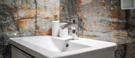 A bathroom with a white sink, chrome faucet, and marble-patterned walls.