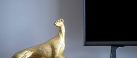 Una estatua dorada de un gato sobre una superficie de madera, junto a un televisor.
