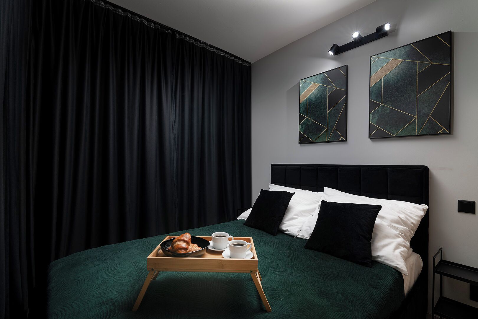 A modern hotel room with a large bed, dark curtains, and two abstract paintings on the wall.