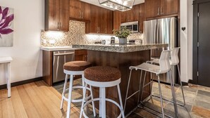 A modern kitchen with dark wood cabinets, stainless steel appliances, a granite countertop, and two bar stools. - Stunning Silver Creek 1Br Mtn view penthouse (Canmore)