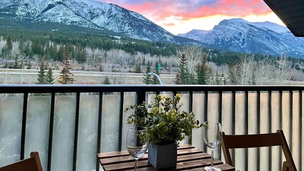 A balcony with a view of snow-covered mountains and a sunset. - Stunning Silver Creek 1Br Mtn view penthouse (Canmore)