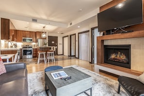 A modern living room with a fireplace, a kitchen in the background, and a dining area with stools.