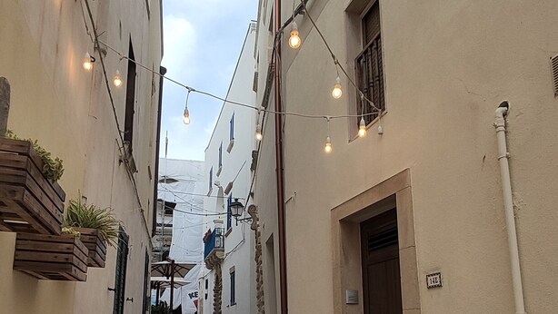 A cobblestone street in a narrow alley with buildings on either side, string lights, and a sign that reads "KE". - Apartment in the heart of Otranto (Otranto)