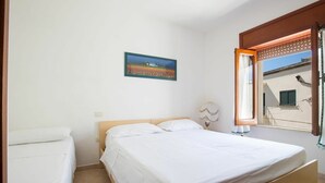 A bedroom with a bed, a bedside table, a lamp, a window with blinds, and a painting on the wall. - Apartment in the heart of Otranto (Otranto)