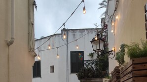 A cobblestone street with buildings on either side, string lights overhead, and a stone wall with a wooden planter. - Apartment in the heart of Otranto (Otranto)