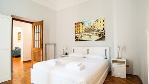 A neatly made bed with white linens and towels, a painting of a cityscape on the wall, and a wooden floor. - Imperial House  (Roma)