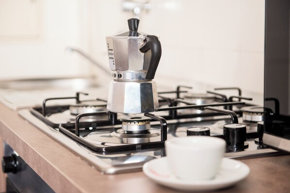 A kitchen with a gas stove, a coffee maker, and a cup on the counter.