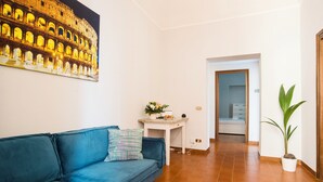 A living room with a blue sofa, a small table with a plant, and a wall-mounted picture of the Colosseum. - Imperial House  (Roma)