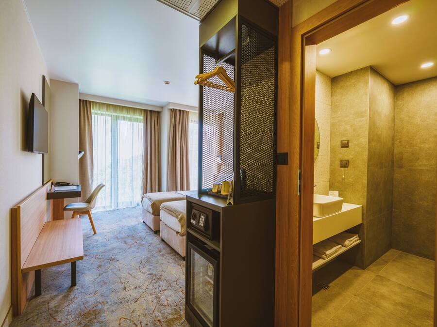 A hotel room with a desk, chair, bed, and a bathroom with a sink and shower.