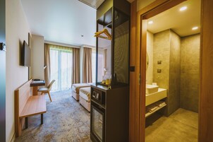 A hotel room with a desk, chair, bed, and a bathroom with a sink and shower.