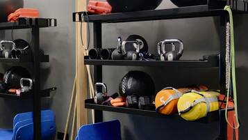 Un gimnasio con equipo de ejercicio, incluyendo pesas rusas, balones medicinales y una colchoneta azul.