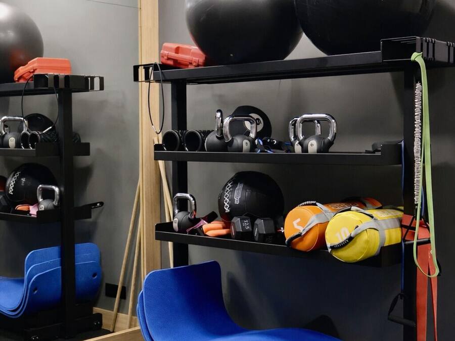 Un gimnasio con equipo de ejercicio, incluyendo pesas rusas, balones medicinales y una colchoneta azul.