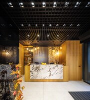 Un área de recepción con mostrador de mármol, paneles de madera y techo con diseño de cuadrícula y luces empotradas.