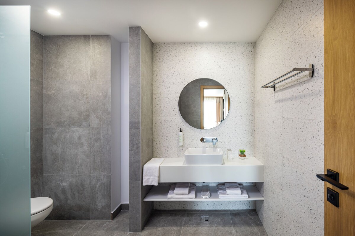 A modern bathroom with a shower, a sink, a mirror, and a towel rack.