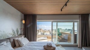 A modern hotel room with a large bed, a city view through a sliding door, and a wooden ceiling. - Penthouse, pool & Valletta views | ROP by Homega (Sliema)