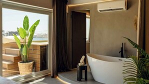 A modern bathroom with a freestanding bathtub, a potted plant, and a view of a cityscape through a large window. - Penthouse, pool & Valletta views | ROP by Homega (Sliema)