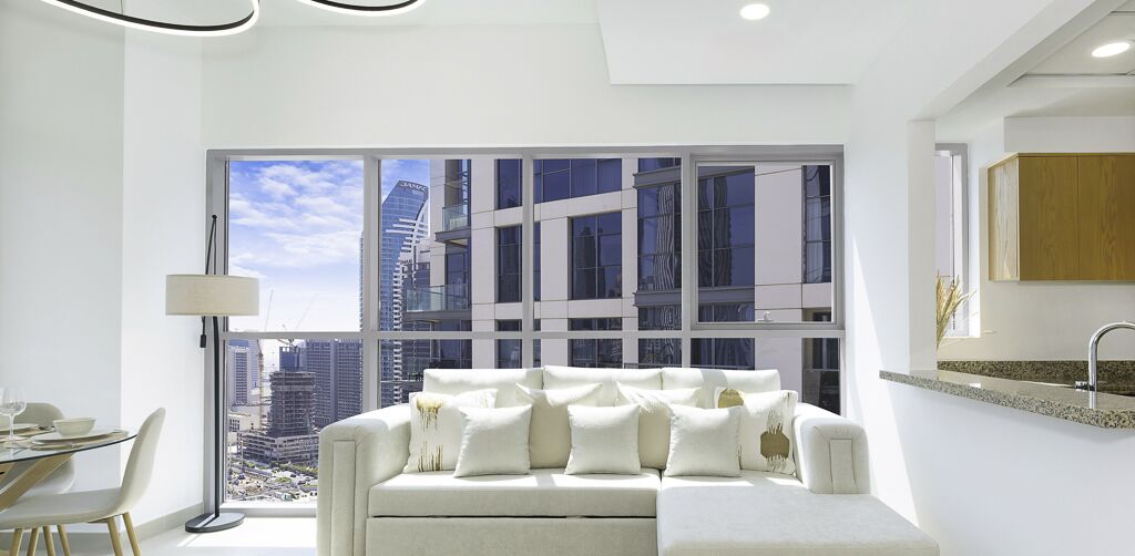 Un salón moderno con un sofá blanco, una mesa de comedor con sillas y un ventanal con vistas a la ciudad.