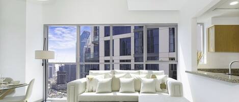 Un salón moderno con un sofá blanco, una mesa de comedor con sillas y un ventanal con vistas a la ciudad.