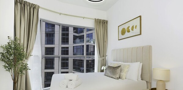 A hotel room with a bed, a window with curtains, a plant, and a framed picture on the wall. - LUX Executive Burj Khalifa View Suite (Dubai)
